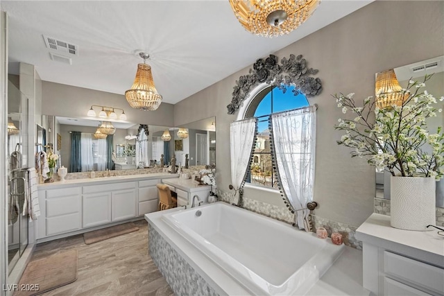 bathroom with vanity, a chandelier, and tiled bath