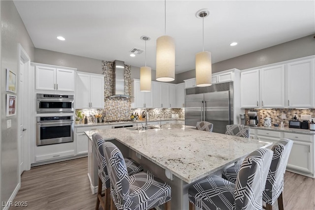 kitchen with appliances with stainless steel finishes, a kitchen breakfast bar, an island with sink, and wall chimney range hood