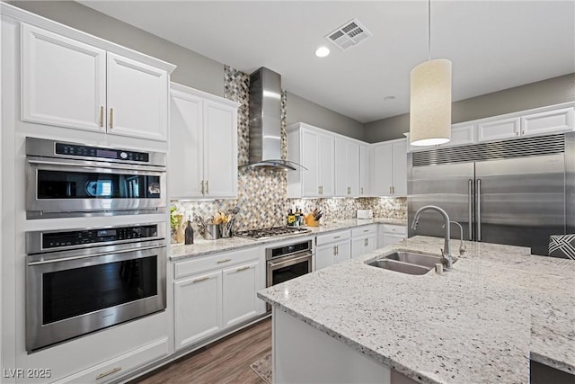 kitchen with hanging light fixtures, wall chimney range hood, white cabinetry, appliances with stainless steel finishes, and sink