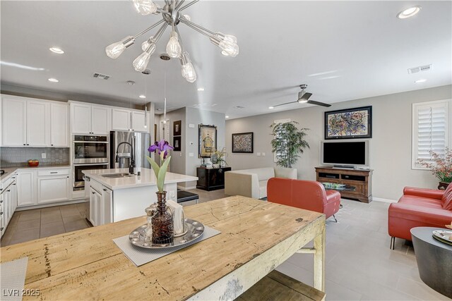 kitchen with a kitchen island with sink, appliances with stainless steel finishes, white cabinetry, decorative light fixtures, and ceiling fan with notable chandelier