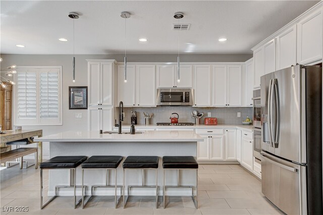 kitchen featuring pendant lighting, an island with sink, white cabinets, appliances with stainless steel finishes, and sink