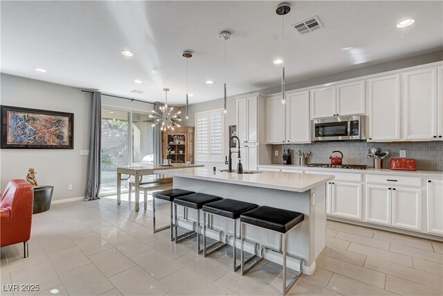 kitchen featuring white cabinets, hanging light fixtures, a kitchen island with sink, and sink