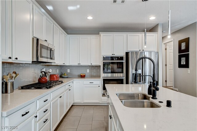 kitchen featuring hanging light fixtures, stainless steel appliances, white cabinetry, light tile patterned flooring, and sink