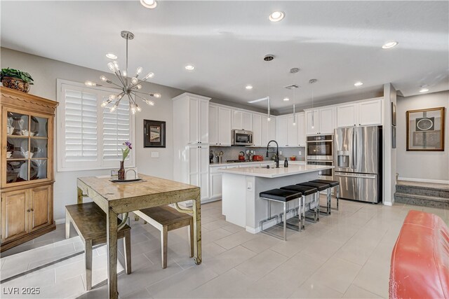 kitchen with decorative light fixtures, stainless steel appliances, a kitchen island with sink, and white cabinets