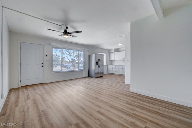 unfurnished living room with beamed ceiling, ceiling fan, and light hardwood / wood-style flooring