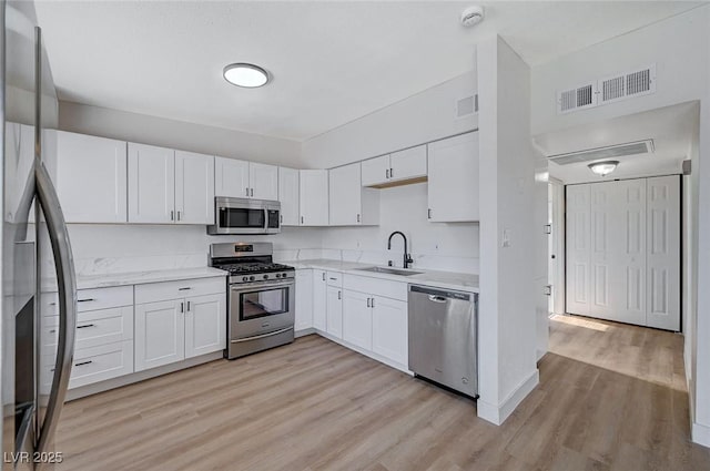 kitchen with sink, stainless steel appliances, white cabinetry, and light hardwood / wood-style floors