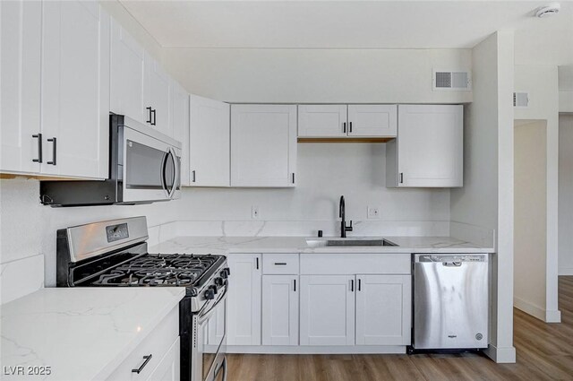 kitchen featuring stainless steel appliances, white cabinets, sink, and light stone counters