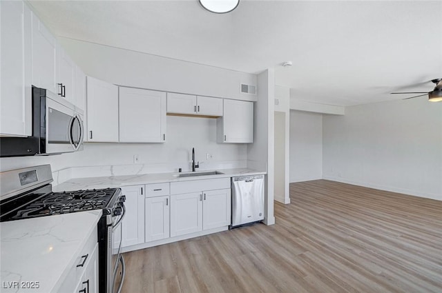 kitchen with stainless steel appliances, light stone countertops, white cabinetry, and sink