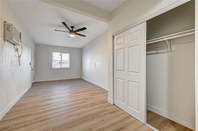 unfurnished bedroom with an AC wall unit, light wood-type flooring, ceiling fan, and a closet