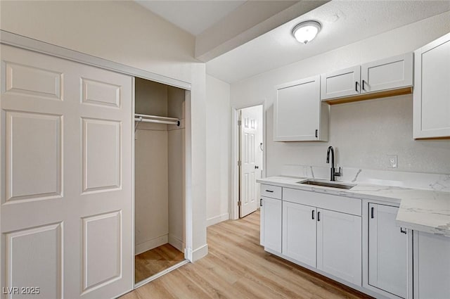 kitchen with light stone countertops, sink, white cabinets, and light hardwood / wood-style flooring