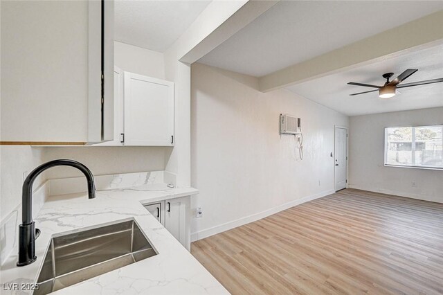 kitchen with light stone countertops, light wood-type flooring, white cabinets, ceiling fan, and sink