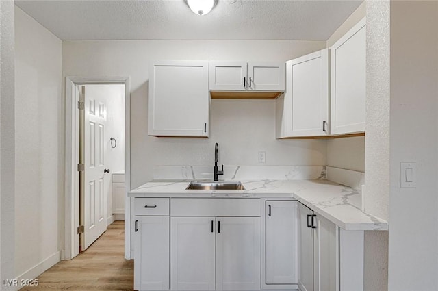 kitchen with light stone countertops, sink, white cabinets, and light hardwood / wood-style flooring