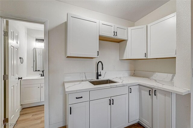 kitchen featuring white cabinets, light stone countertops, a textured ceiling, sink, and light hardwood / wood-style flooring