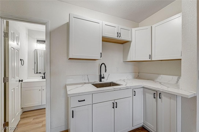 kitchen with sink, light stone countertops, a textured ceiling, white cabinets, and light wood-type flooring