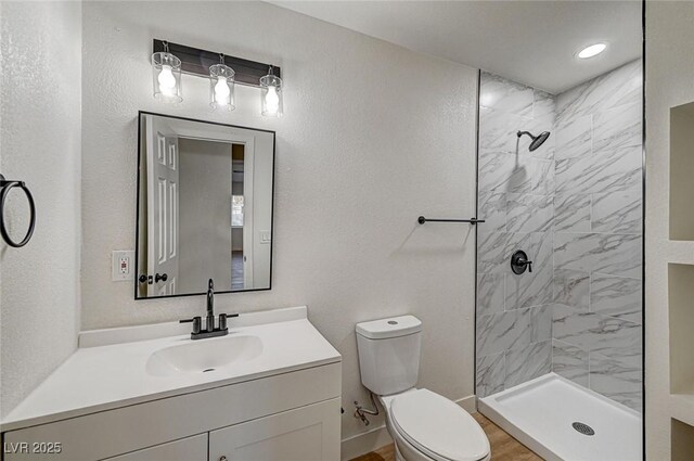 bathroom with toilet, a tile shower, and vanity