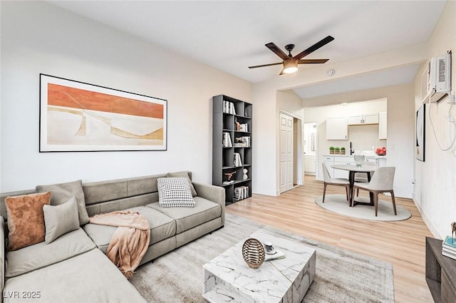 living room featuring a wall mounted air conditioner, ceiling fan, and light wood-type flooring