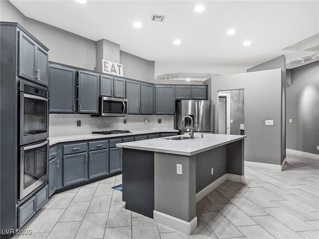 kitchen featuring gray cabinets, stainless steel appliances, an island with sink, sink, and tasteful backsplash