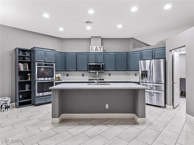 kitchen featuring stainless steel appliances, decorative backsplash, a kitchen island with sink, blue cabinetry, and sink