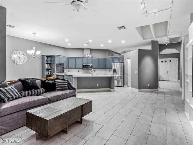 living room featuring ceiling fan with notable chandelier, rail lighting, and sink