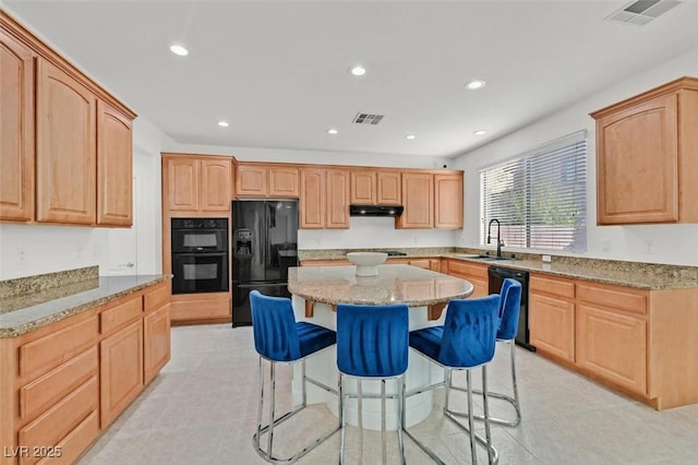 kitchen with sink, a center island, light stone counters, a kitchen breakfast bar, and black appliances