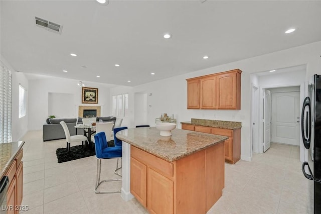 kitchen featuring black refrigerator, a center island, light tile patterned floors, a kitchen bar, and light stone counters