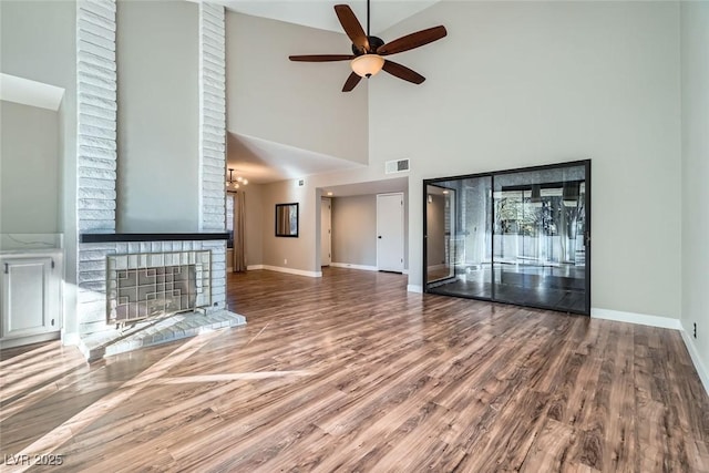 unfurnished living room featuring ceiling fan with notable chandelier, a fireplace, high vaulted ceiling, and hardwood / wood-style floors