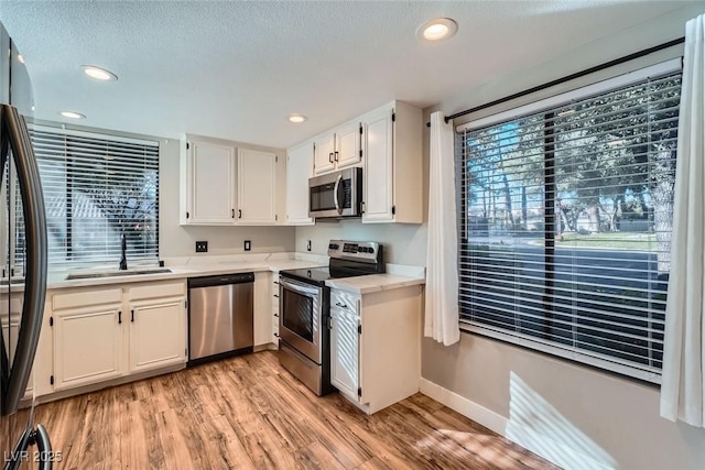 kitchen featuring sink, stainless steel appliances, light hardwood / wood-style flooring, and white cabinets