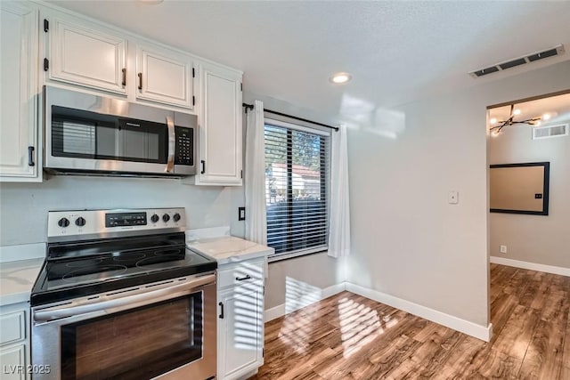 kitchen with stainless steel appliances, a notable chandelier, white cabinets, and hardwood / wood-style floors