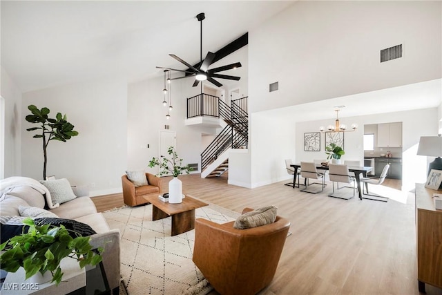 living room featuring light hardwood / wood-style flooring, high vaulted ceiling, and ceiling fan with notable chandelier