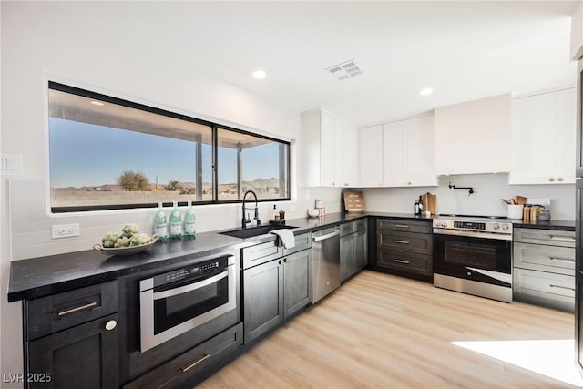 kitchen with custom exhaust hood, light hardwood / wood-style floors, white cabinetry, appliances with stainless steel finishes, and sink