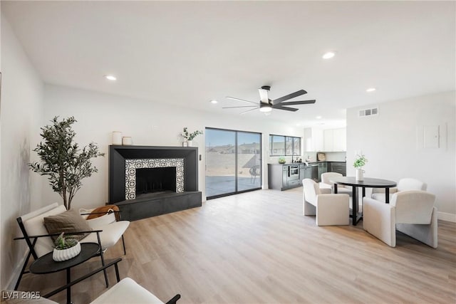 living room with ceiling fan, light wood-type flooring, and a tiled fireplace