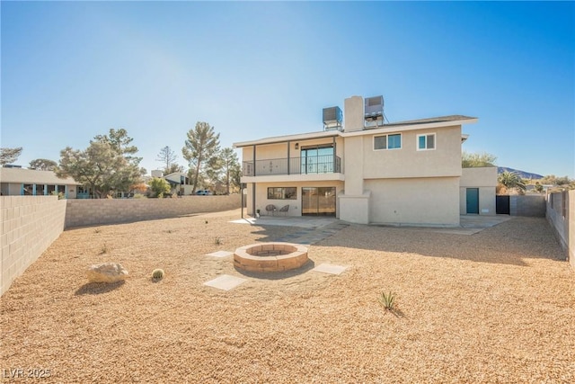 rear view of property featuring a balcony, central AC unit, an outdoor fire pit, and a patio area