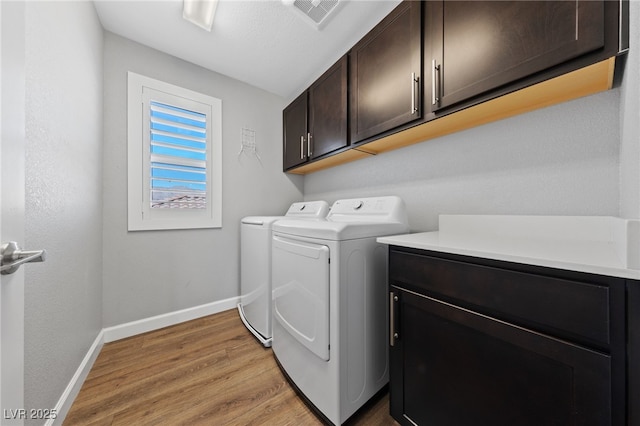 washroom featuring cabinets, washing machine and dryer, and light wood-type flooring