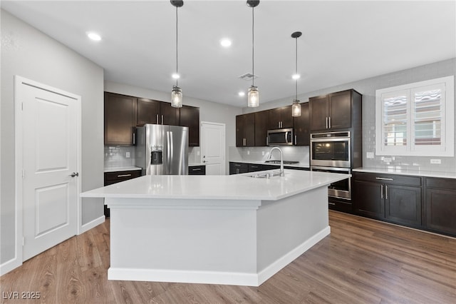 kitchen with stainless steel appliances, dark brown cabinets, a kitchen island with sink, and hanging light fixtures