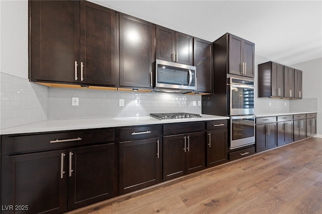 kitchen featuring light wood-type flooring, appliances with stainless steel finishes, backsplash, and dark brown cabinetry