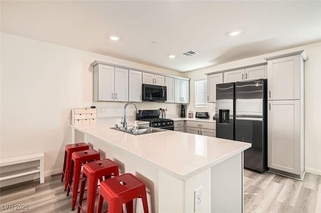 kitchen with kitchen peninsula, stainless steel fridge, a breakfast bar area, black range with gas stovetop, and sink