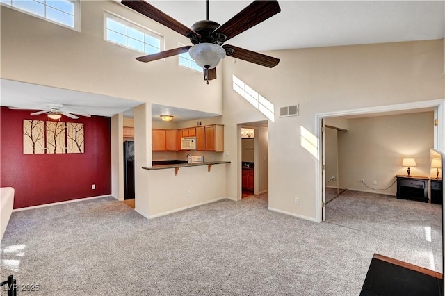 unfurnished living room with a high ceiling, ceiling fan, and light carpet