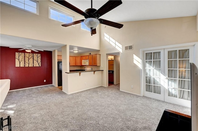 unfurnished living room featuring a towering ceiling, french doors, ceiling fan, and light colored carpet