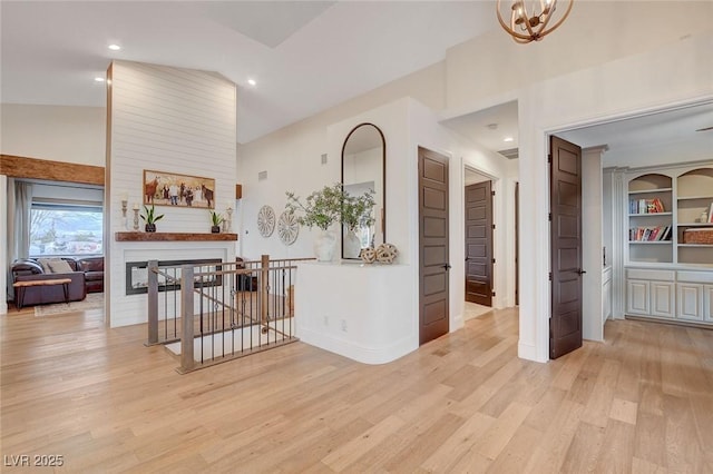 hall with light wood-type flooring, an inviting chandelier, high vaulted ceiling, and built in shelves