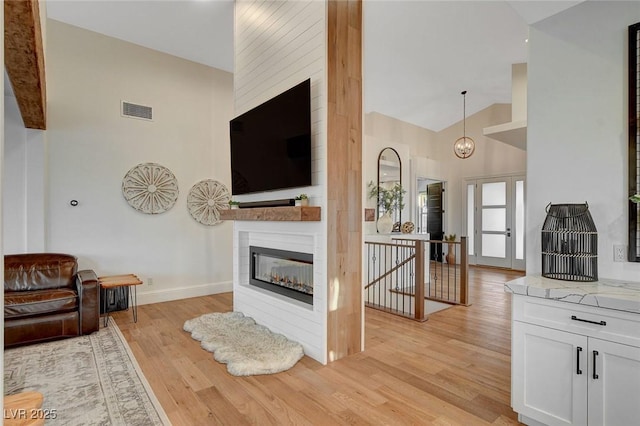 living room with lofted ceiling, a large fireplace, and light hardwood / wood-style flooring