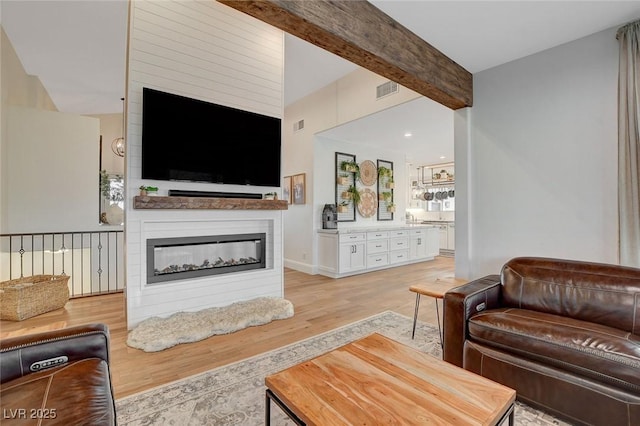 living room featuring a large fireplace, light hardwood / wood-style flooring, and beamed ceiling