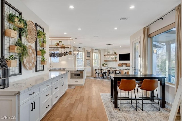 kitchen with white cabinetry, light wood-type flooring, a wealth of natural light, light stone countertops, and a kitchen island