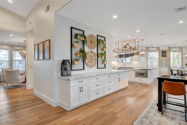 kitchen with light hardwood / wood-style floors, a healthy amount of sunlight, white cabinetry, and light stone counters