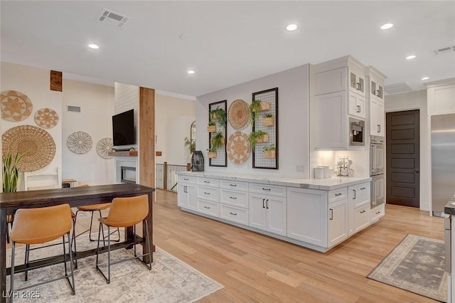 kitchen with white cabinets, light wood-type flooring, light stone countertops, and a large fireplace