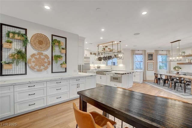 kitchen featuring light stone counters, light hardwood / wood-style flooring, decorative light fixtures, stainless steel appliances, and white cabinets