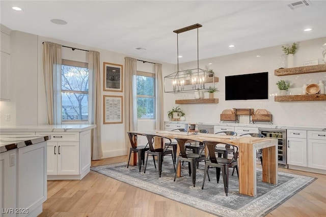 bar with light hardwood / wood-style flooring, a chandelier, decorative light fixtures, beverage cooler, and white cabinets