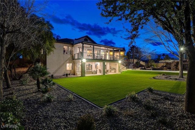 back house at dusk with a lawn, a balcony, and a patio