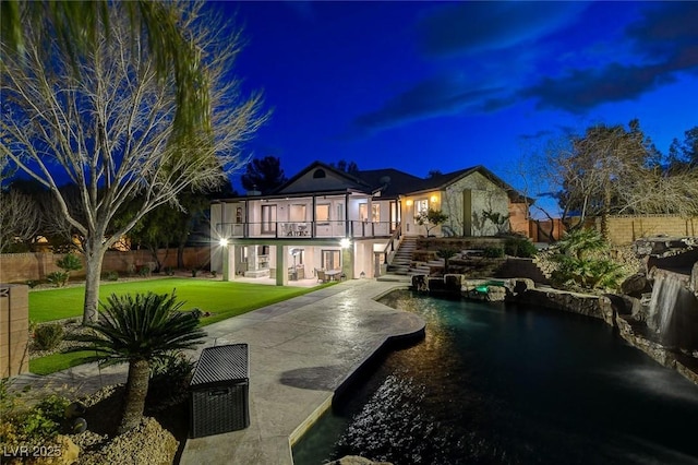 back house at twilight featuring a balcony, a patio area, a yard, and a fenced in pool