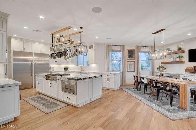 kitchen featuring appliances with stainless steel finishes, hanging light fixtures, light stone counters, light hardwood / wood-style flooring, and white cabinetry