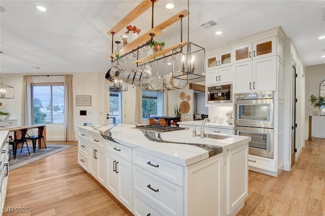 kitchen with sink, decorative light fixtures, a kitchen island with sink, and white cabinets